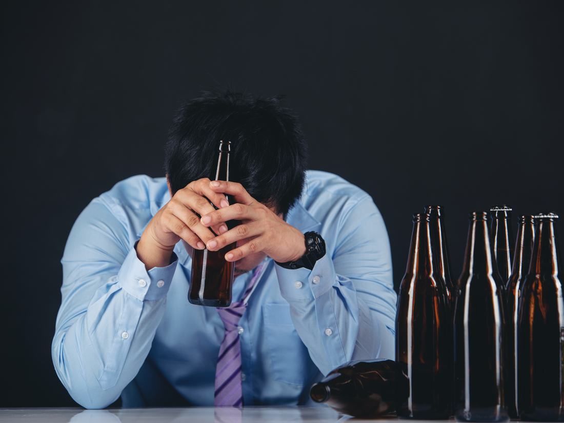 A man at a table of empty beer bottles with his head in his hands