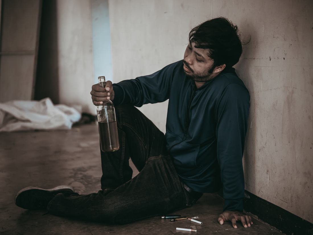 A man alone on the floor with a bottle beside him