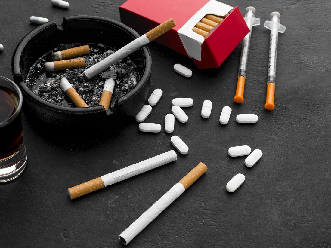 A full ashtray beside an open cigarette packet and loose cigarettes